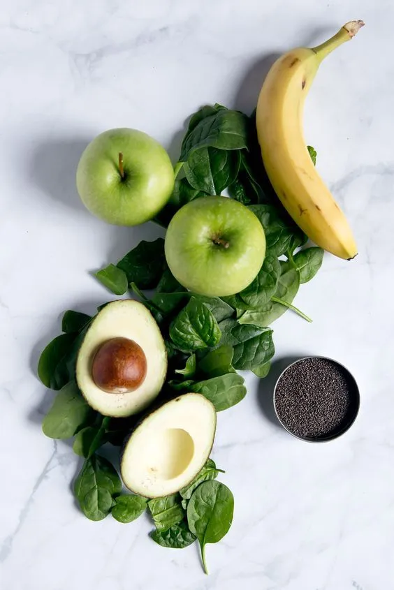 Avocado tagliato a metà, mele verdi, banana, foglie di spinacio e semi di chia su un piano di marmo